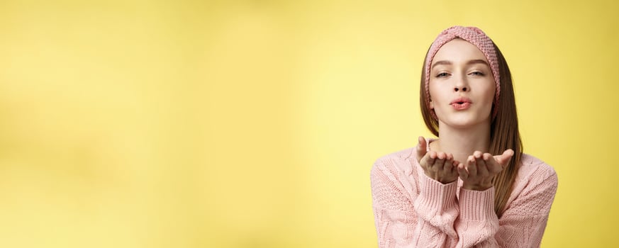Happy valentines day. Charming romantic and sensual young flirty woman in knitted headband, sweater extending palms near folded lips sending air mwah, blowing kiss tender and gentle photo