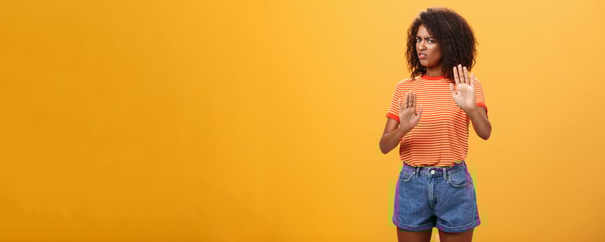 No I refuse. Intense suspicious and displeased smart african-american female rejecting bad offer pulling raised palms turning away with aversion and dissatisfied look against orange background photo