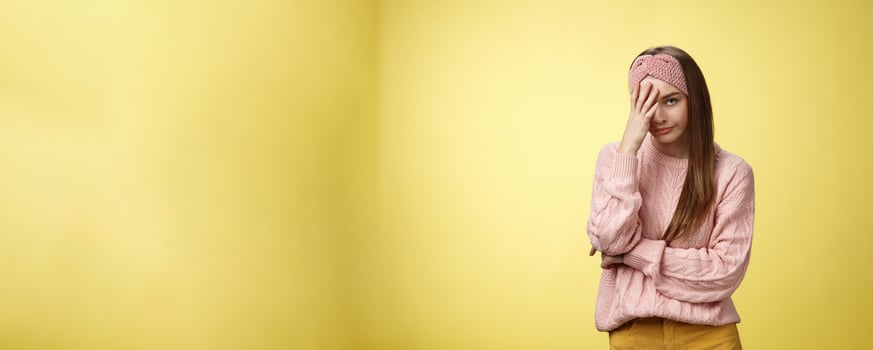 Woman facepalming covering face annoyed, bothered and inrritated, smirking looking with dismay, pissed off, posing unhappy displeased, staring indignant and upset posing tired over yellow background photo