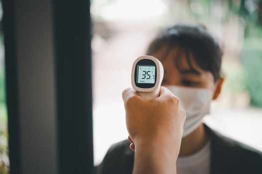 Hand holding infrared thermometer to measuring temperature people with face mask on background. Covid flu screening 19 concept. photo
