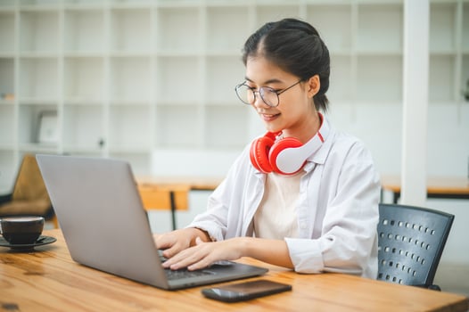 Student using a laptop in a cafe while wearing headphones, learning and searching the internet, and making a call. photo