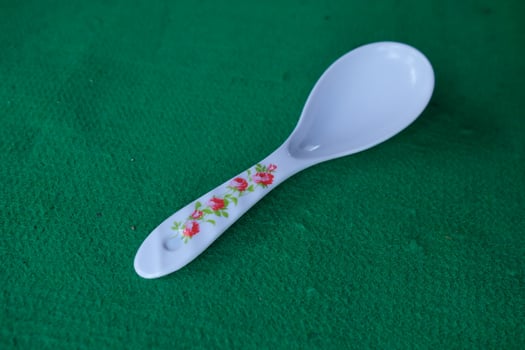 White spoon with floral design on a green surface. photo