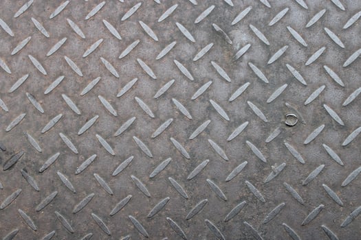 Close-up of textured metal surface with diamond pattern and a single screw. photo