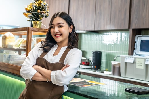 Welcoming guests, Portrait of cheerful young asian professional barista or businesswoman owning bakery in brown apron welcoming customers near cashier, Attractive model posing photo