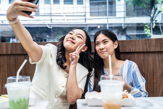 Two young asia females taking selfie using mobile phone while sitting in the cafe, Two joyful attractive Asian girls together at restaurant or cafe. Holiday activity, or modern lifestyle concept photo