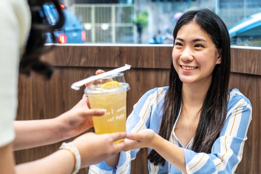 Waiter serving glass of fresh juice to a customer who was a young asian woman on table in the restaurant, Juice bar employees serving drink to customer, good service, Good-natured atmosphere photo