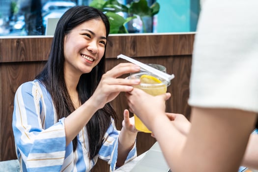 Waiter serving glass of fresh juice to a customer who was a young asian woman on table in the restaurant, Juice bar employees serving drink to customer, good service, Good-natured atmosphere photo