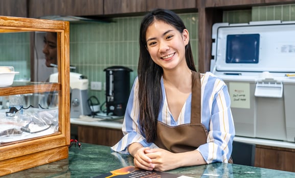 Welcoming guests, Portrait of cheerful young asian professional barista or businesswoman owning bakery in brown apron welcoming customers near cashier, Attractive model posing photo