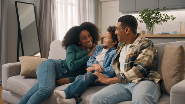 Excited happy smiling African American ethnic family woman little boy strong man bringing new sofa couch furniture apartment then mother father son sitting hugging relaxing enjoying rest indoors home photo
