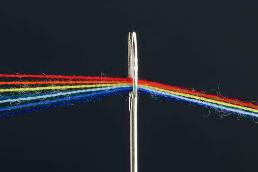 multi-colored threads for sewing in the form of a rainbow pass through an antique needle on a black background photo