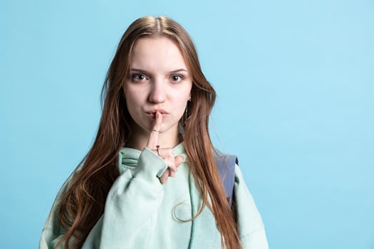 Upset young teenager doing shushing hand gesturing, irritated by loud noises, requesting silence. Irked person placing finger on lips, doing quiet sign gesture, giving criticism, studio backdrop photo