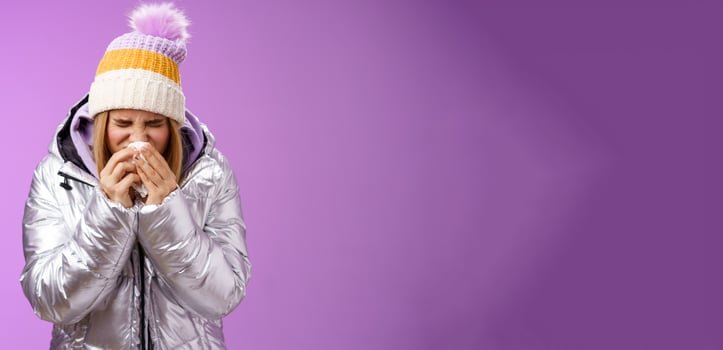 Girl runny nose sneeze tissue press napkin face got ill feeling unwell sick heading hospital standing purple background bending wearing silver stylish jacket winter hat, crying sobbing photo