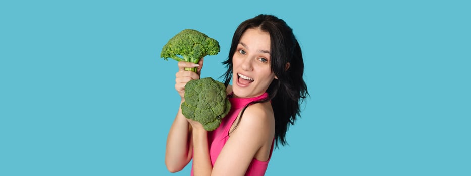 Caucasian young woman holding fresh broccoli on a blue background. Panorama, a place for text photo