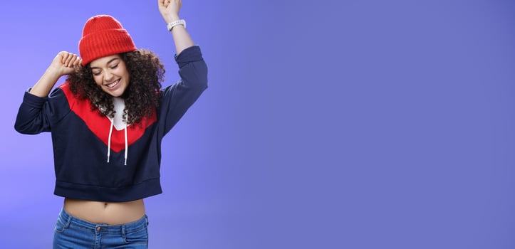 Girl celebrating favorite season in year. Portrait of carefree and joyful dancing woman with curly hair in cute red hat lifting hands in dance movements smiling enjoying music and holidays photo