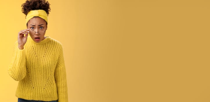 Shocked amazed african-american female student drop jaw gasping concerned confused take-off glasses bending forward reassure see truth, standing impressed speechless, yellow background photo