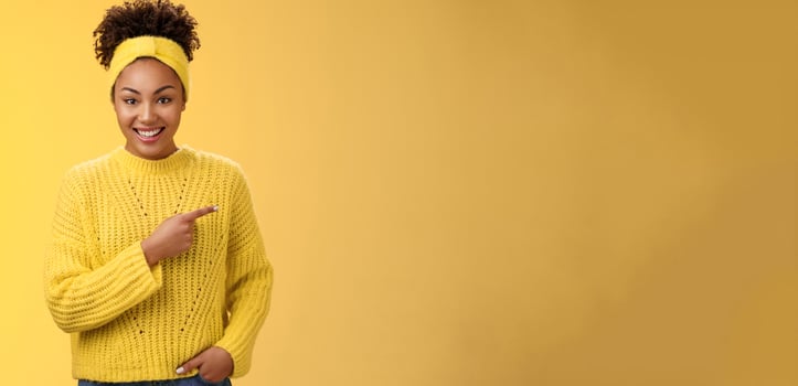 Friendly ougoing relaxed african-american woman casually pointing right during conversation discussing recent new cafe open awesome discounts promos standing happily yellow background photo