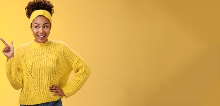 Charming tender young easy-going millennial stylish girl in sweater hold hand waist confident pointing looking impressed upper left corner smiling broadly ineterested, curiously discussing product photo