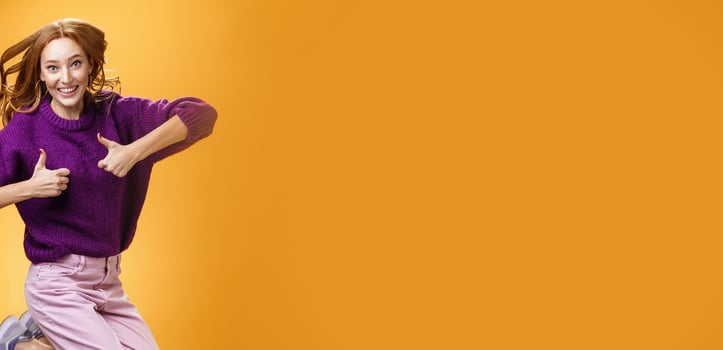Optimistic and cheerful woman liking promotion lifting thumbs up and jumping from excitement and delighted, having fun recommending good idea smiling thrilled and enthusiastic over orange background photo