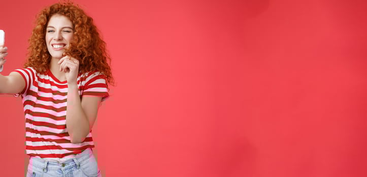 Sassy good-looking stylish charismatic redhead female curly hairstyle winking cheeky expression making flirty kinky faces hold smartphone taking selfie record message play funny facial filters photo
