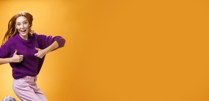 Excited and happy funny young redhead female in purple sweater jumping from happiness and satisfacion showing thumbs up gesture in approval giving positive reply and liking awesome clothes photo