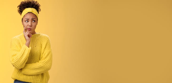Perplexed unsure cute timid african-american female thinking how escape awkward situation smirking frowning concerned touch cheek thoughtful thinking nervously, worried yellow background photo