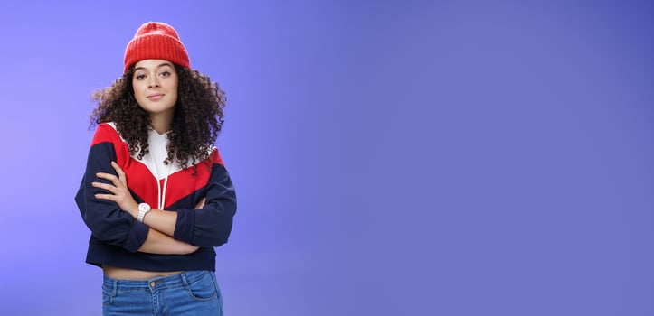 Girl will show winter who boss. Confident and stylish self-assured attractive woman with curly hair in cute red beanie and warm sweatshirt holding hands crossed over chest and looking daring at camera photo