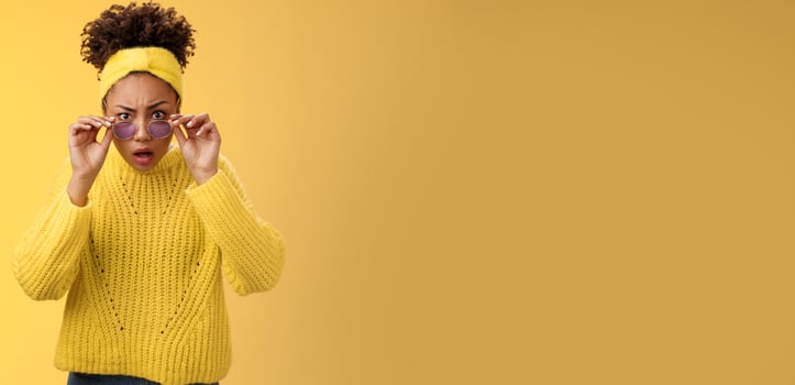 Shocked speechless impressed african-american stylish female coworker drop jaw look amazed take-off sunglasses widen eyes cannot believe confused standing yellow background questioned stare camera photo