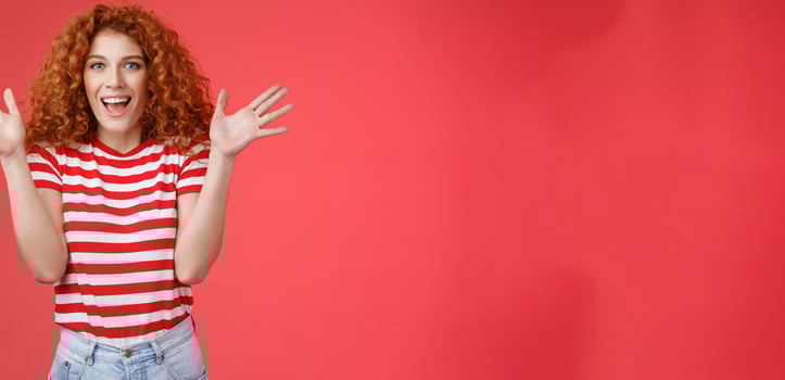 Awesome incredible performance bravo. Attractive cheerful cute european redhead curly female raise hands thrilled express excitement happiness joy look camera entertained delighted red background photo