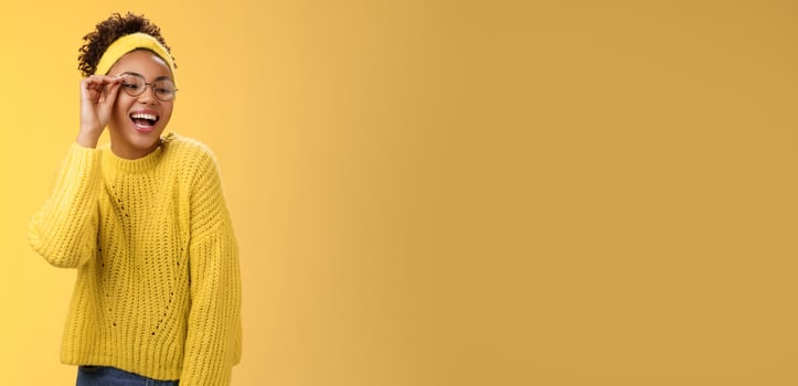 Charismatic stylish confident beautiful african-american joyful teenage girl touching glasses nose laughing broadly look down right corner grinning have fun joking enjoying, yellow background photo