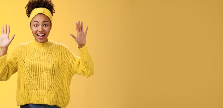 Charming excited smiling friendly millennial african-american girl raise hands nothing hide show palms high surrender standing amused thrilled grinning having fun posing yellow background photo