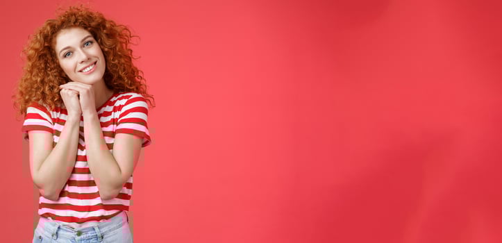 Tender feminine caring redhead curly-haired female romantic gaze camera tilt head clench palms near head silly lovely look smiling delighted cheerful dreamy sighing look with sympathy photo