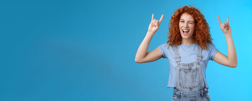 Daring cool sassy redhead ginger girl curly natural hairstyle winking joyfully yelling yeah enjoy awesome party dancing music festival show rock-n-roll heavy metal gesture have fun blue background photo