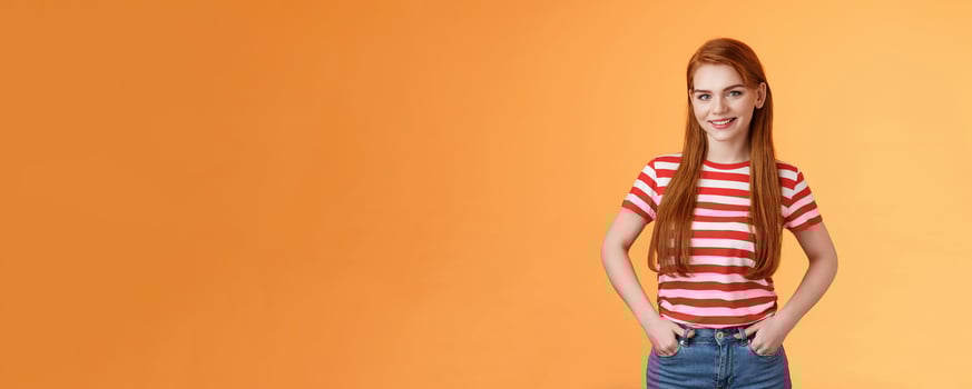 Skillful motivated cheerful redhead woman hold hands pants smiling empowered, professional entrepreneur grinning satisfied managing business alone, good start-up, orange background photo