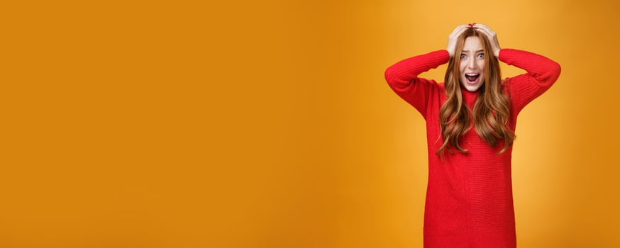 Girl goes insane from pressured panicking feeling tensed and troubles yelling from anxiety, worries being in difficult situation holding hands on head popping eyes, posing concerned over orange wall photo