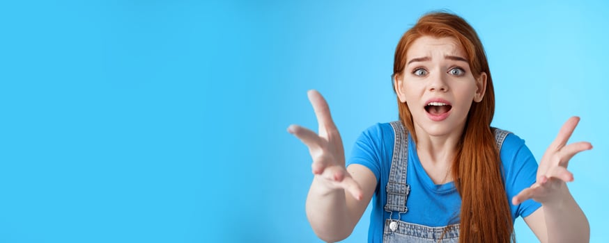 Close-up uneasy disappointed cute gloomy redhead girl, raise hands dismay full dibelief, frowning gasping upset, losing competition, receive bad results, stand blue background unhappy photo