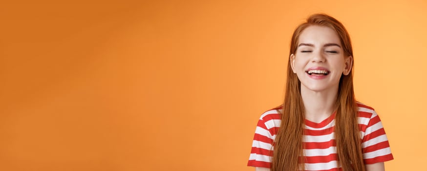 Sincere happy charismatic redhead girl smiling, close eyes enjoy warm summer sunbeams, laughing cheerful, feel relaxed rejoicing, show white teeth, good vacation concept, orange background photo