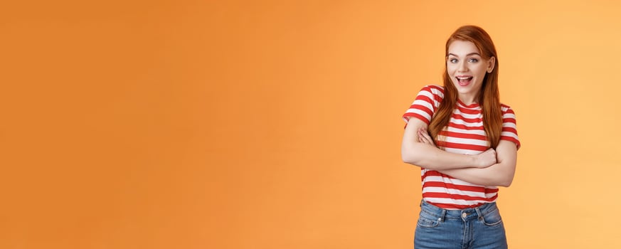 Excited cheerful ginger girl long natural red hair open mouth enthusiastic smile, cross arms chest, gladly react interesting awesome news, feel surprised pleased, stand orange background photo