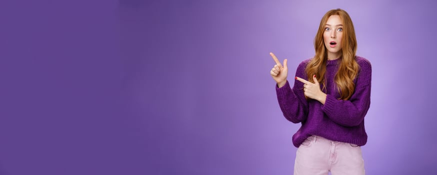 Stunned girl asking friend if she saw it drop jaw from stupor and amazement popping eyes at camera after witnessing shocking revelation pointing questioned at upper left corner over purple wall photo