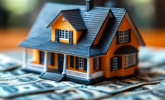 A small house is sitting on top of a pile of money. The house is orange and black, and it looks like it's made of plastic. photo