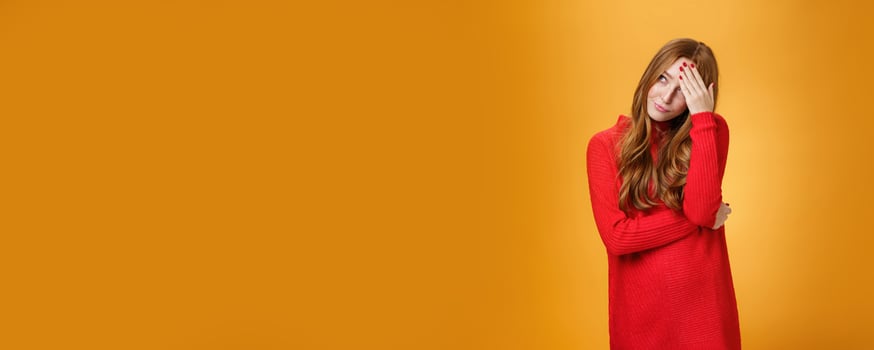Annoyed and pissed embarrassed woman hiding behind hand making facepalm gesture looking away with irritated humiliated gesture, standing fed up and intense against orange background photo