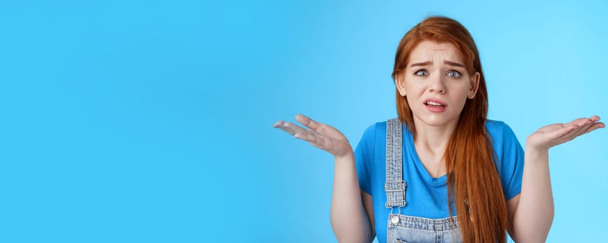 Perplexed uneasy stupified worried redhead woman shrugging, have no idea, frowning nervously, cannot understand what happened, stand clueless unsure, pose blue background photo