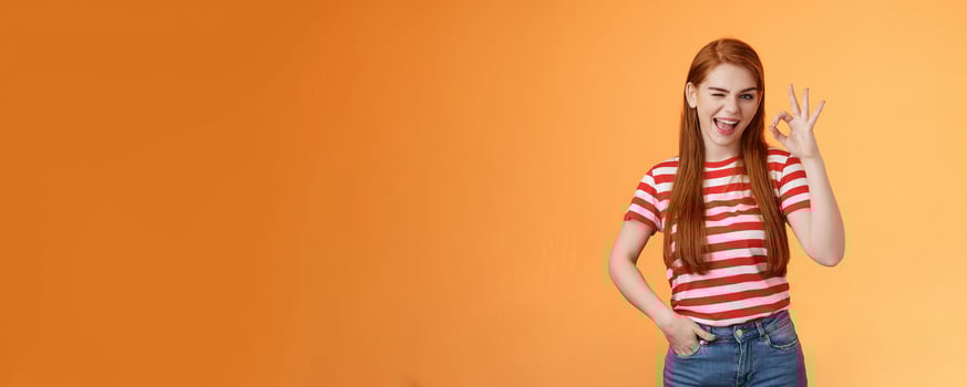 Sassy stylish sly redhead cheerful girl assuring everything excellent, show okay sign and wink cheeky, accept awesome idea, approve good job, express satifaction from positive result, like choice photo