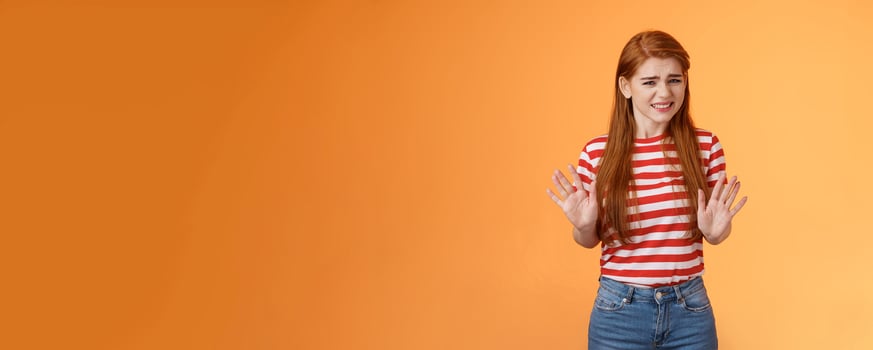 Reluctant bothered cute redhead girl apologizing make stop refusal sign, hold hands block, grimacing, cringe unwilling participate, rejecting offer, stand orange background uncomfortable, step back photo