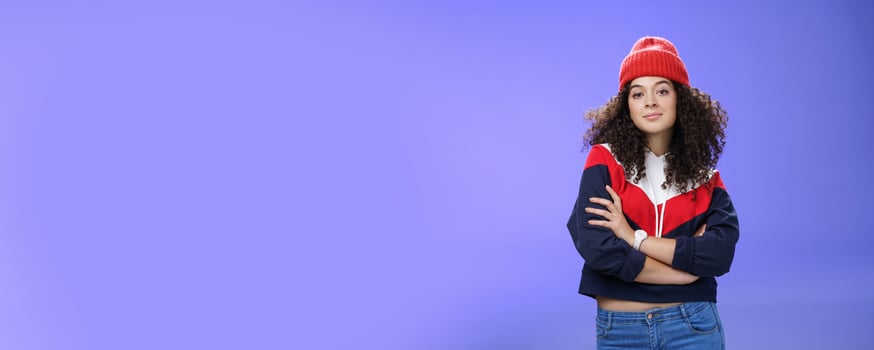 Girl will show winter who boss. Confident and stylish self-assured attractive woman with curly hair in cute red beanie and warm sweatshirt holding hands crossed over chest and looking daring at camera photo