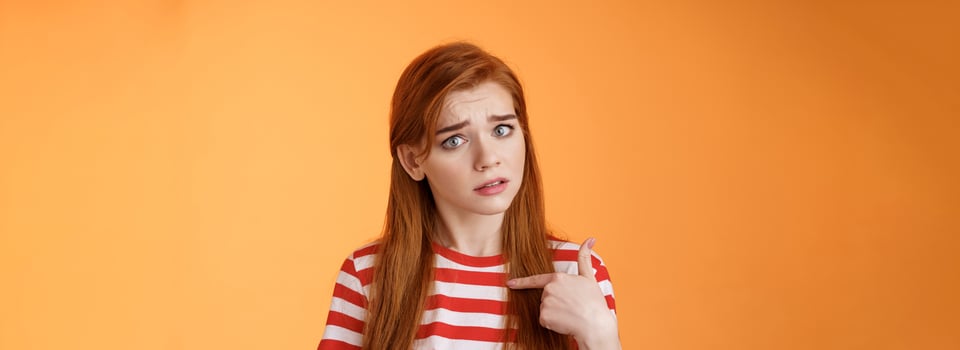 Offended innocent timid redhead girl hurt feelings, hear upsetting accusations, pointing herself frowning, look insulted, grimace frustrated, stand uneasy bothered orange background photo