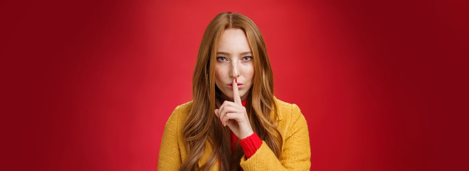 Shh keep out secret safe. Portrait of sensual attractive and daring redhead female in yellow coat showing shush gesture with index finger on lips, squinting looking determined and sassy over red wall photo