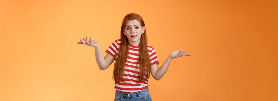Careless arrogant redhead rich girl say so what, not giving care what people thing, look dismay ignorant shrugging hands spread sideways, uninterested, give no concern, stand orange background photo