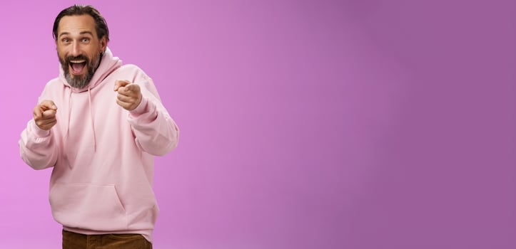 Gotcha. Portrait carefree funny amusing adult energized bearded man jumping pranking friend having fun laughing happily pointing camera index fingers greeting picking you, purple background photo