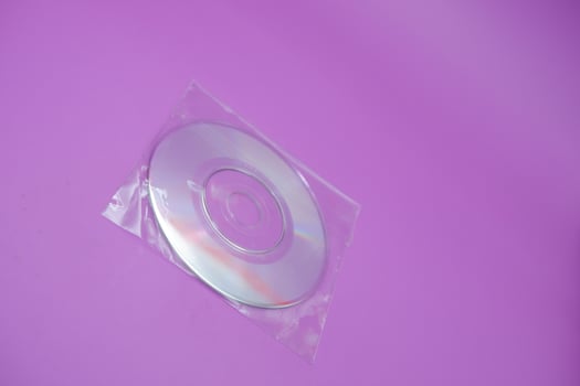A compact disc isolated on a purple background. A compact disc wrapped in clear plastic. photo