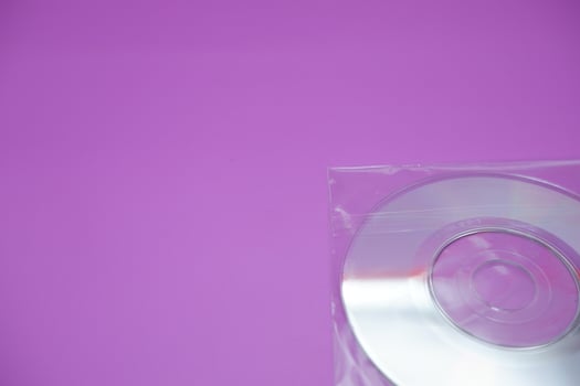 A compact disc isolated on a purple background. A compact disc wrapped in clear plastic. photo